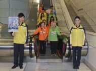 身穿港鐵制服的張子丰及林千豔，聯同鄭欣宜、Regen、胡鴻鈞及As One，與長者示範如何正確使用扶手電梯。